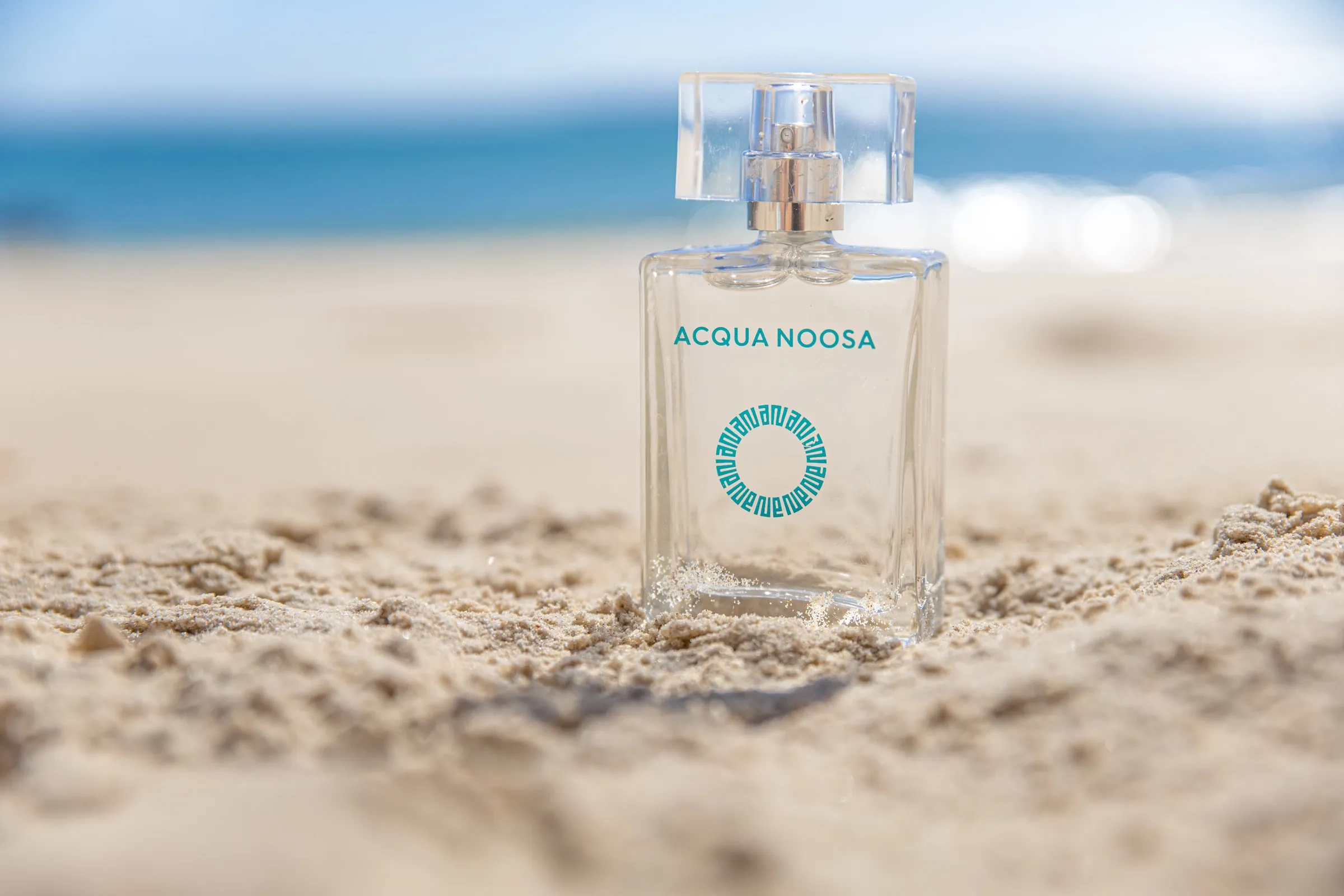 The 50ml bottle standing in beach sand with the ocean behind it